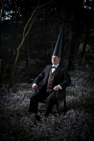 surreal man in conemen sitting on a chair wearing a suit in a forest at night